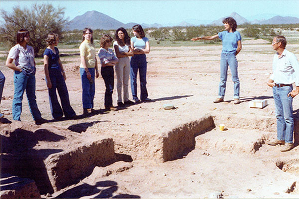 A group of people stand and observe a piece of excavated land in an archival photo