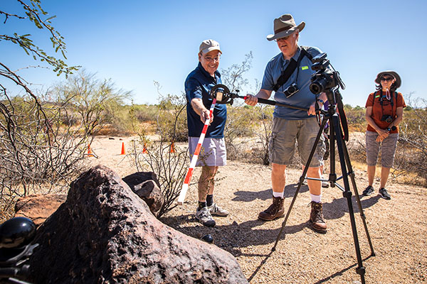 Three people use tools to measure and view rock art