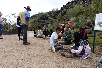 A group of children sitting outside while a volunteer gives directions